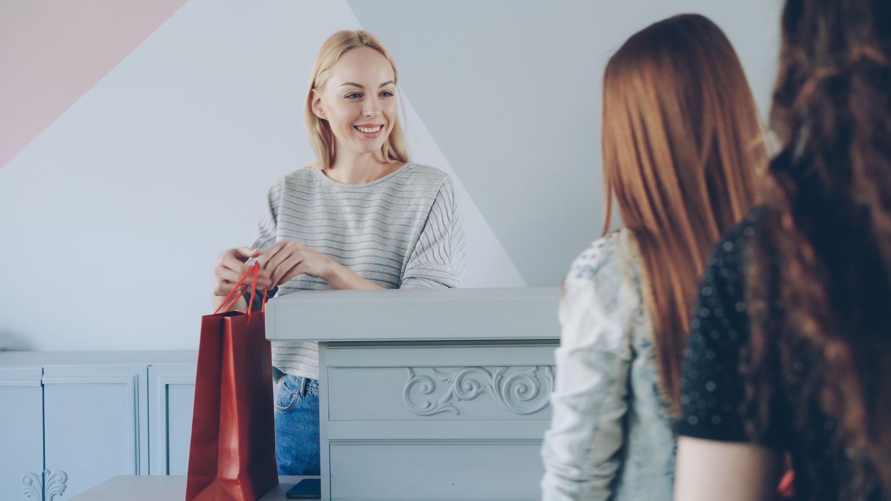 A shop assistant handing a customer a shopping bag across the counter.