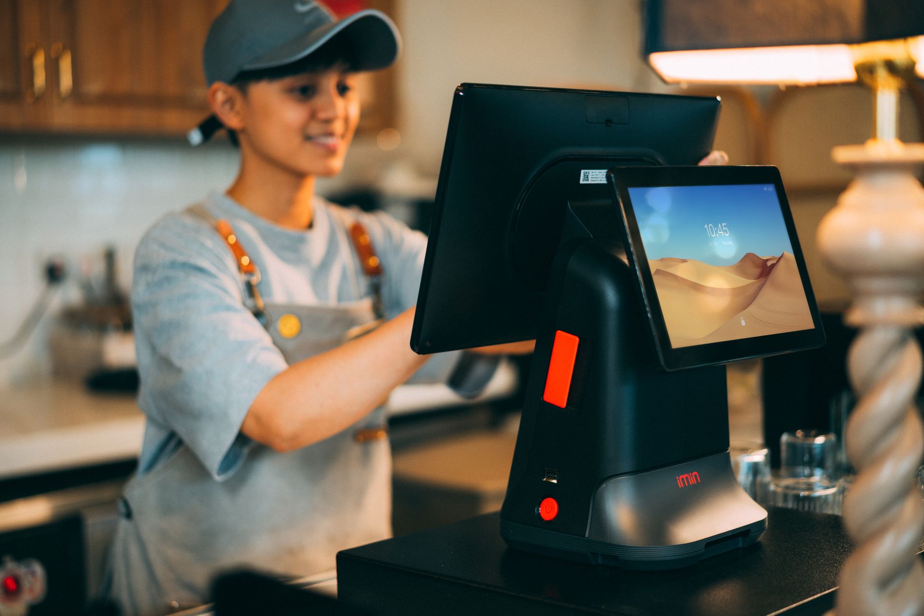 A shop assistant turning the customer-facing screen of a countertop point-of-sale terminal.
