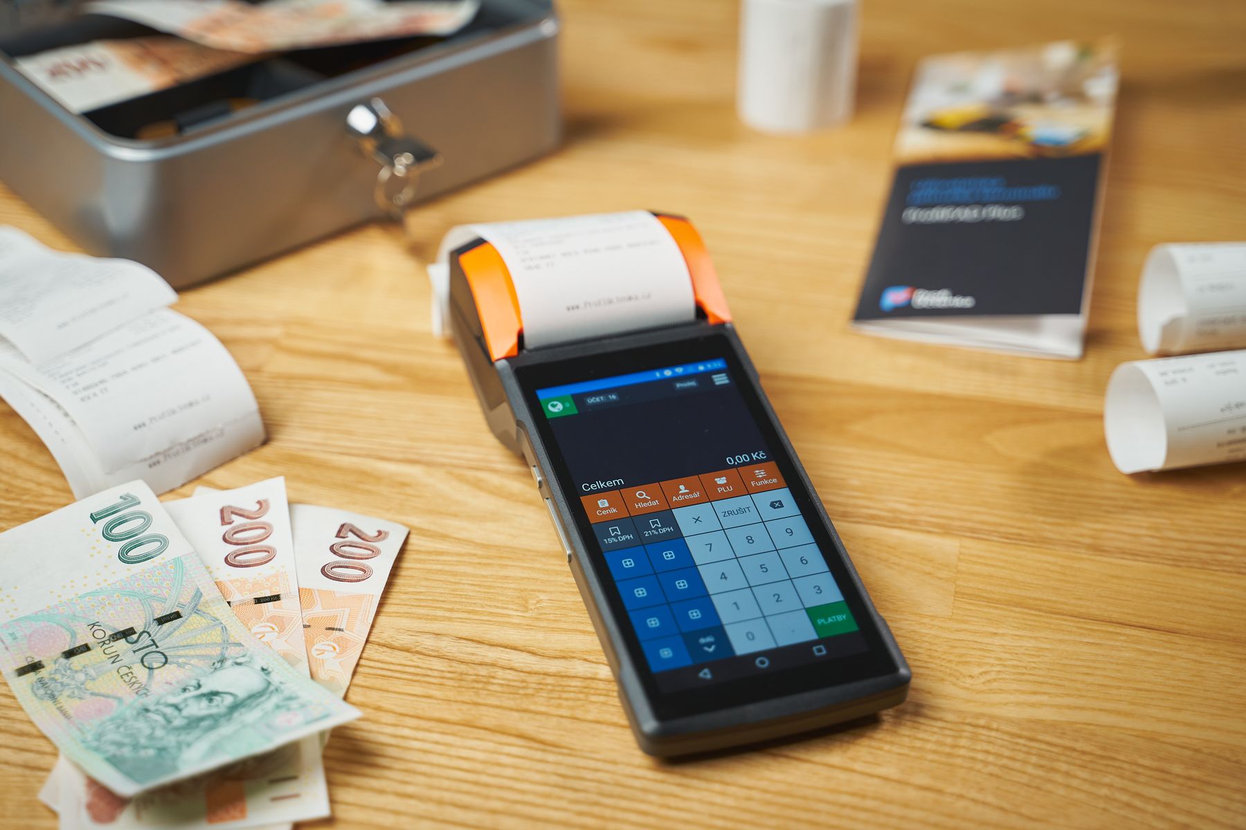 A card terminal, banknotes and printed receipts on a wooden desk.
