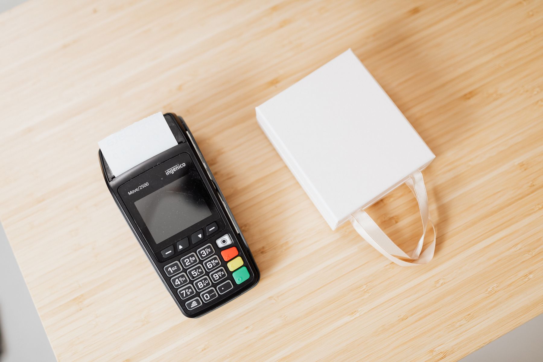 A card terminal with a printed receipt beside a plain paper bag on a counter.